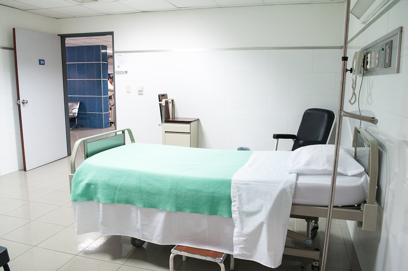 An empty, clean hospital room with a made bed beside a window