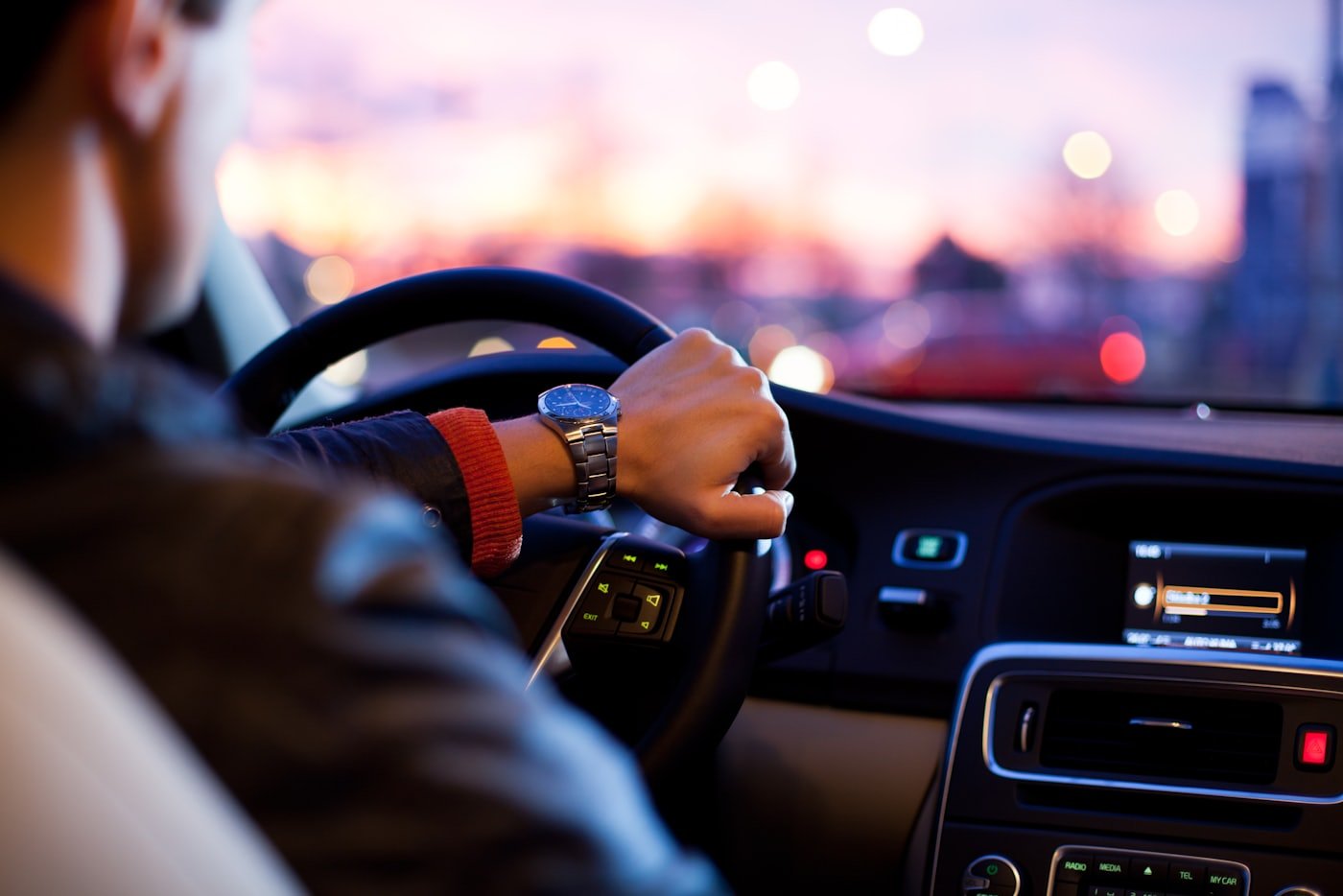 A driver's hands resting on a car steering wheel at dusk